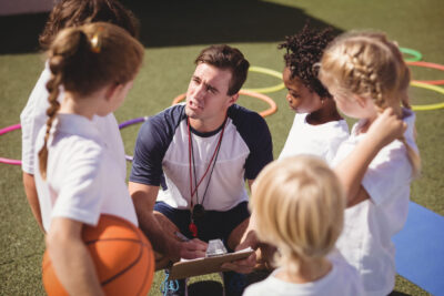 Coach,And,Schoolkids,Discussing,On,Clipboard,In,Schoolyard